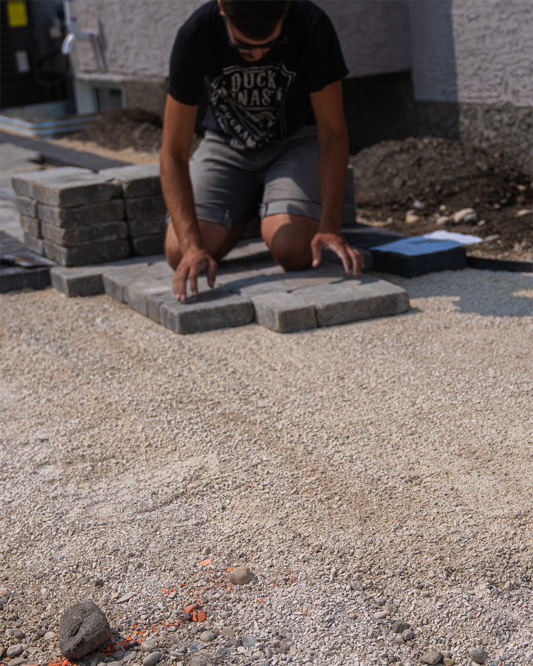 Man laying hardscape brick patio on top of crushed limestone outside of a home