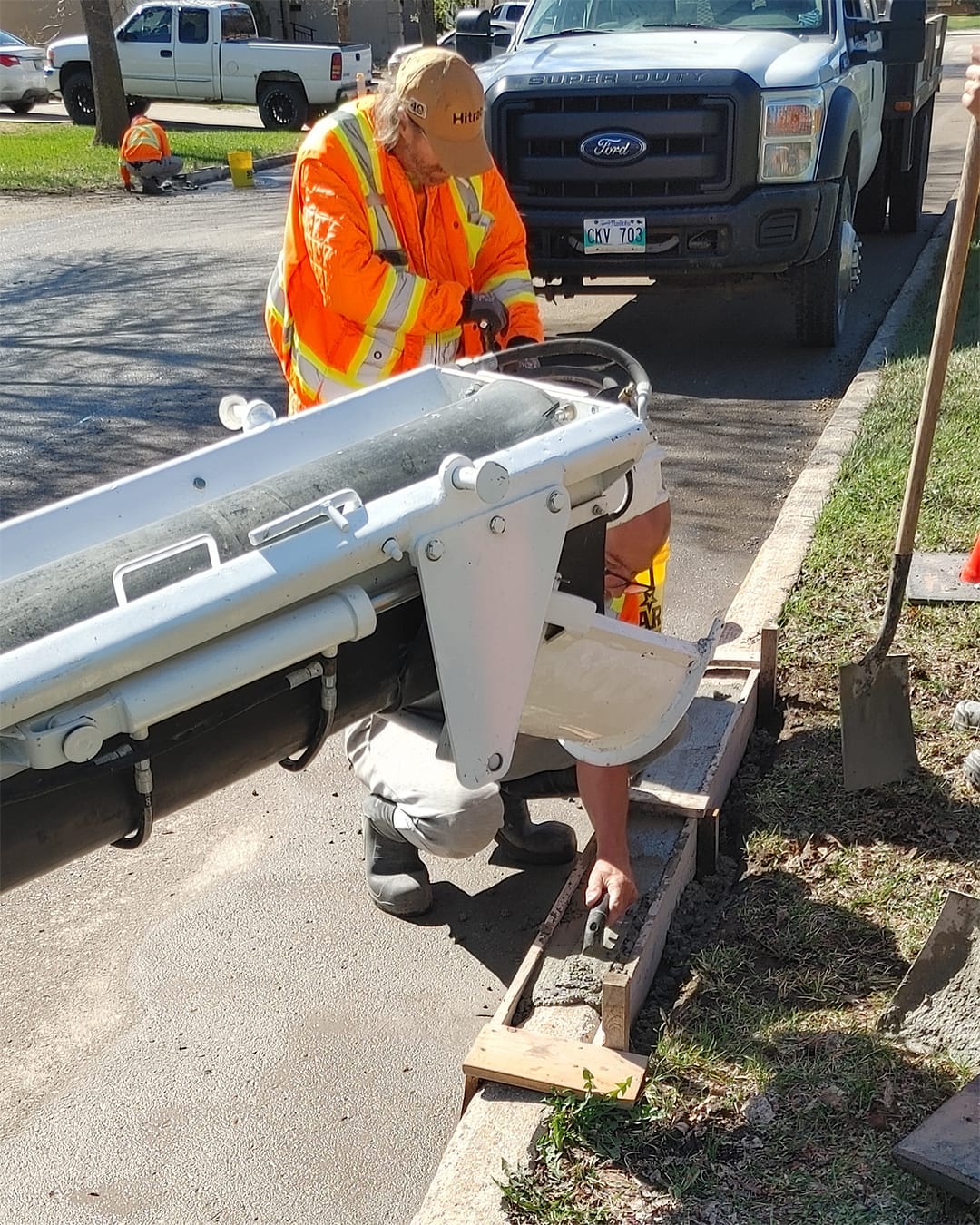 Two men operate an on-site concrete mixer for curb repair on a residential road